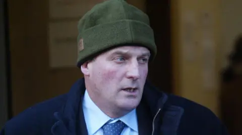 PA Media Hector Dick outside court. He is wearing a green beanie hat, a dark blue coat and a light coloured shirt with a blue tie.