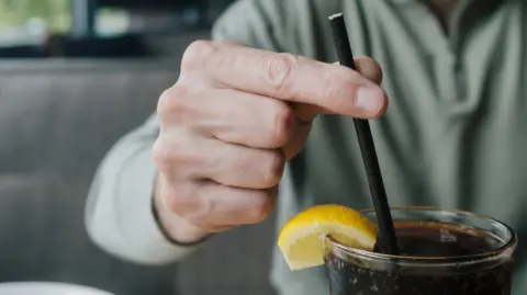 A man holding a straw standing in a glass of pop.