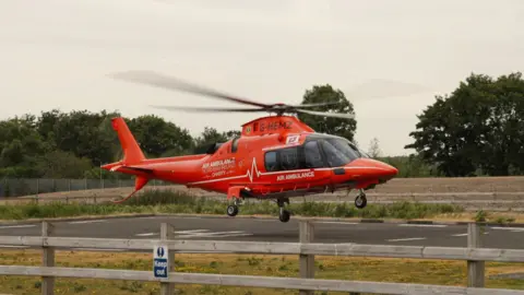 NI Air Ambulance An Air Ambulance helicopter hovering above the ground with the rotor blades blurry from spinning fast