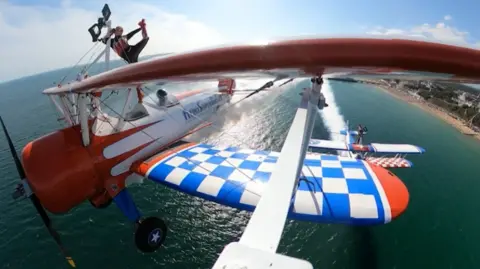 Kirsten Pobjoy /  AeroSuperBatics Wing-walkers performing on two bi-planes over a body of water