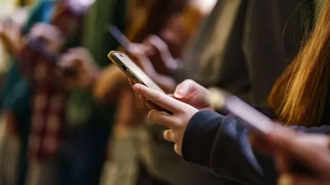 Getty Images A group of young people looking at their smartphones.