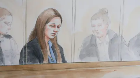 Helen Tipper An artist impression/court drawing of Lucy Letby in the courtroom dock, she looks down and is wearing a black jacket and blue shirt, her hair is down and is long and brown. 