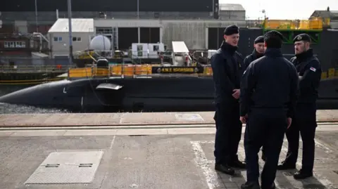 Getty Images Royal Navy personnel standing in a huddle in front of the HMS Agamemnon nuclear submarine.
