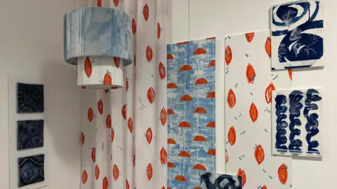 Designs in blue and orange on fabric and boards hung on a wall.