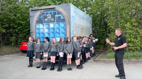 School children stood around a van converted into a 'prison' cell