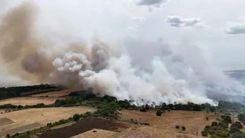 PA Media A drone image that shows huge plumes of black and grey smoke billow from heathland that is on fire. 