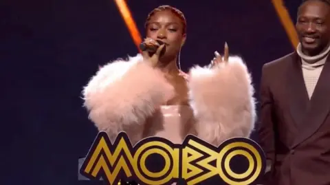 Ayra Starr on stage at a podium at the Mobo Awards