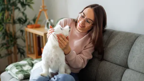 A stock photo of a woman sitting at home with her dog