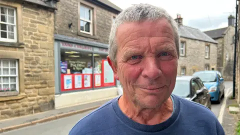 Older man with white hair and a blue top in a village high street