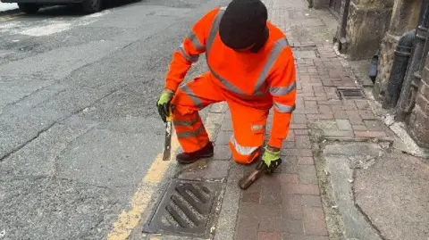 Davinia Ramos/BBC Archie Workman is poised to scrub a drain cover with a wire brush
