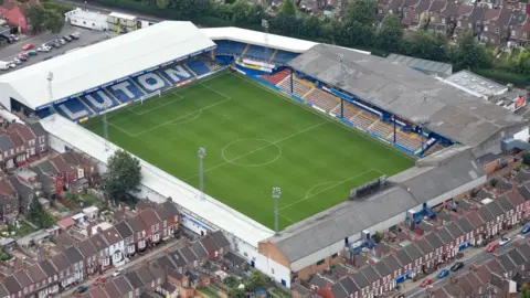 Getty Images An aerial view of Kenilworth Road stadium, showing the green football pitch surrounded by stands and residential houses.