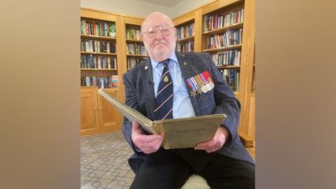 Douglas Parish wearing his medals while reading from his diary