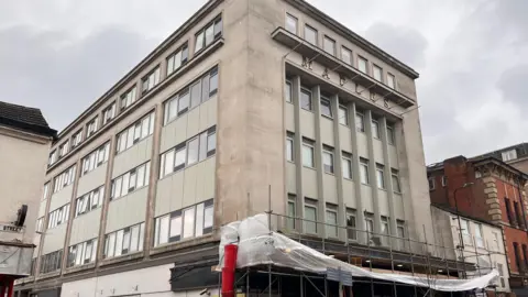 A large white stone five-storey building with scaffolding at ground level
