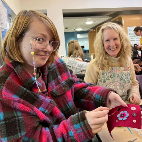 BBC/Naj Modak Student Bailee Wray holds up a piece of cloth with buttons sewn onto it, while Tadcrafters founder Su Morgan looks on.