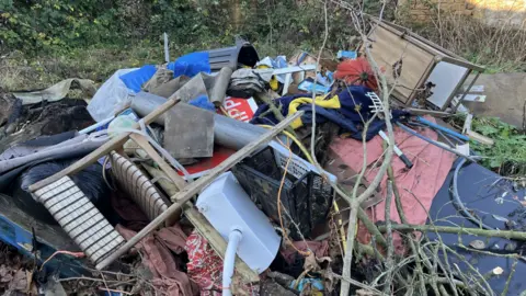 A generic shot showing a pile of waste including chairs, plastic crates, road signs, bins and garden waste.