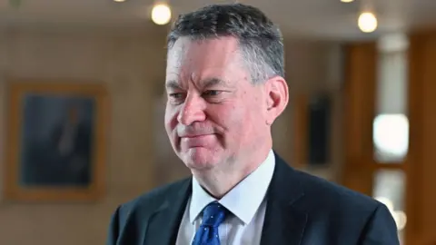 Murdo Fraser, who has short grey hair, wearing a dark suit, white shirt and blue tie. 