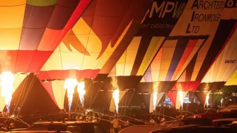 Paul Box A row of hot air balloons glow in the dark as they are lit up by their burners.