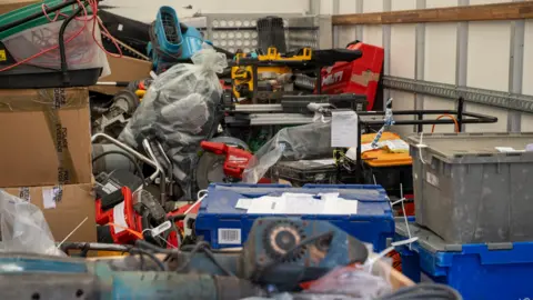 A collection of recovered tools in the back of a lorry. Toolboxes, machinery and lawnmowers can be seen piled up.