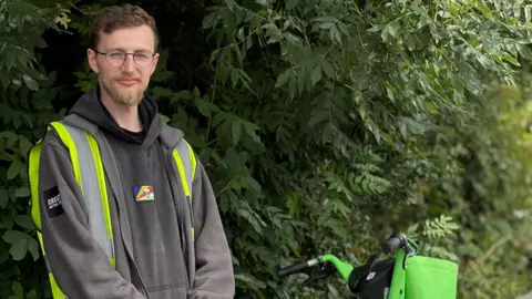 Declan Anthony stood by a ebike in front of some trees