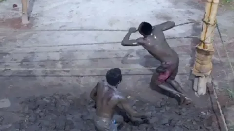 Two people covered in mud move around a wrestling ring