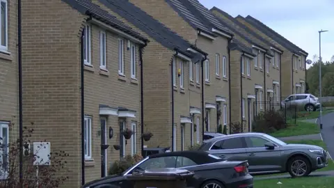 DAVE EDWARDS/BBC A row of 12 houses on a new build estate. Some have cars parked outside.