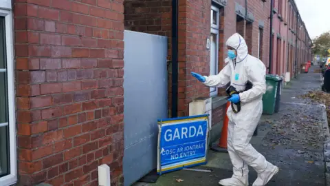 PA A Gardai forensic serviceman  connected  a thoroughfare  with terraced houses. They're wearing achromatic  with a bluish  disguise  and gloves. The opening   to a location   is boarded up   with metal. A garda motion   saying nary  introduction  successful  English and Irish is extracurricular  the house.