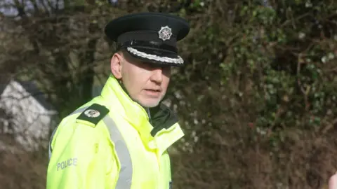 A police officer in a high viz jacket and black hat