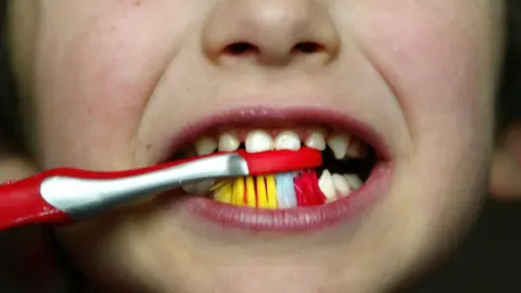 PA Media A close up of a child brushing his teeth with a red and yellow toothbrush.