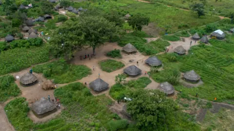 Oxfam An aerial shot of Palabek refugee camp. Thatched roof houses are surrounded by lush greenery