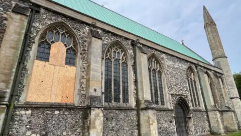 Andrew Turner/BBC An array of the large north-facing windows on St Nicholas Minster; a trio of gothic arched window apertures, with diamond leaded glass set within, featuring a rectangular border. The windows are made of sandstone and set within a flint wall.