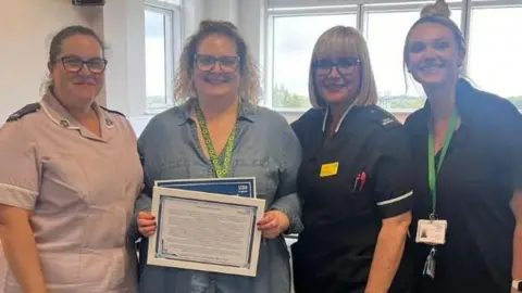 Raynah wearing her blue uniform and black leggings holding her certificate alongside her colleagues 