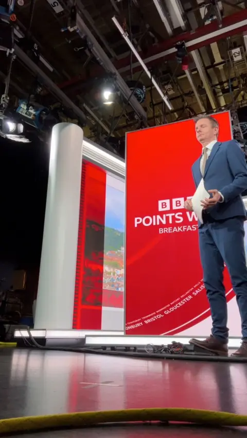 A man standing in front of a red board presenting the news