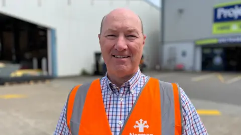 John Bampkin wearing a blue, red and white lined shirt with an orange hi-vis vest on