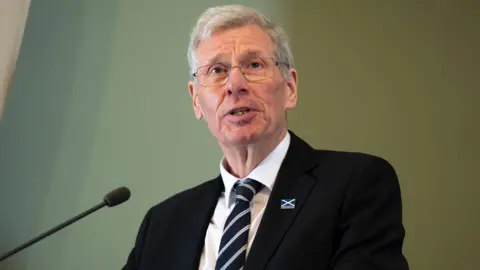 Kenny MacAskill standing at a podium.