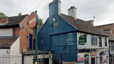 The side view of a two storey building, with a to let sign on the second floor. The  side of the building is painted blue, and most of the letters making up the pub's name are missing