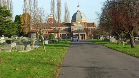 Andrew Smith A tree-lined road through a graveyard with a red-bricked domed building in the background