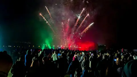 Mark Dotchin Red and green fireworks explode over a large crowd at night, at the Downend Round Table Fireworks Display near Bristol. Rockets are sending multiple spark showers into the sky