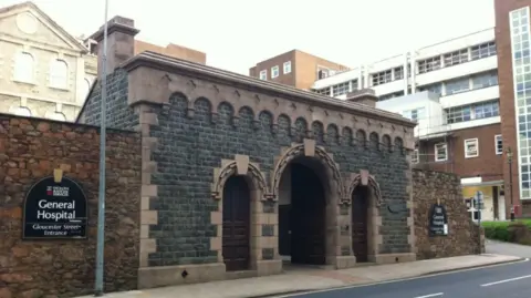 The front of Jersey General Hospital featuring a stone wall and a stone entrance with three archways.