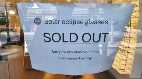 Specsavers Formby Close-up image of a sign on the front door of the high-street opticians Specsavers in Formby which reads: 'Solar eclipse glasses sold out. Apologies for any inconvenience. Specsavers Formby'.