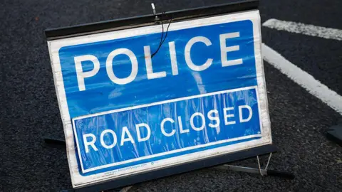 A blue and white sign with the words police, road closed.