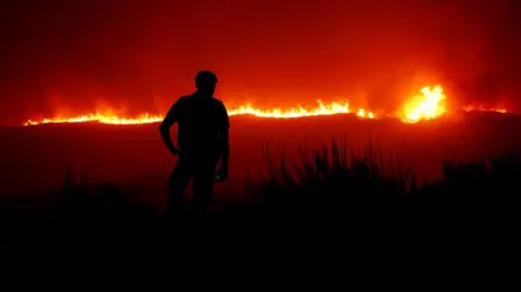 A police officer watches as a wildfire approaches near Povoa de Montemuro