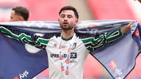 Patrick Roberts, with a flag draped around his shoulders, and a medal around his neck after the play-off final victory.