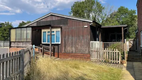 Newbury Men's Shed A one-storey building with wooden planks on the outside and a window. 