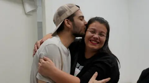 Reuters Yosef-Chaim Ohana wearing a white T-shirt and a beige baseball cap, embaraces and kisses his mother who is smiling