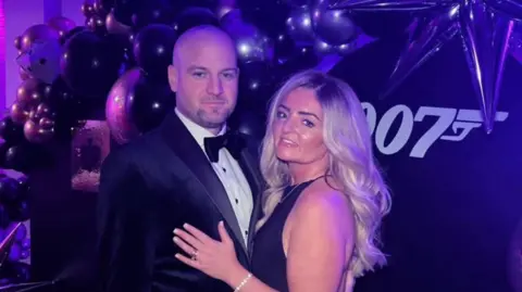 Laura Gregory A couple, wearing black attire for a dinner party, smile and pose for a picture.