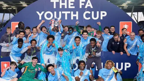 PA Media Manchester City players and staff celebrate with the trophy after they won the FA Youth Cup final at the Joie Stadium