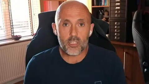 BBC / Harry Craig Ashley Neal sat on an office chair looking directly at the camera face-on while speaking.