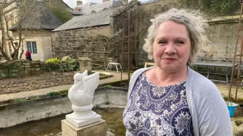 A woman stands in the rose garden at Lamport Hall with the newly installed swan sculpture installed on a plinth