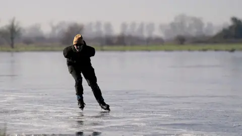 PA Media Ugo Sassi from Cambridge skates on a frozen flooded field in Upware, Cambridgeshire.