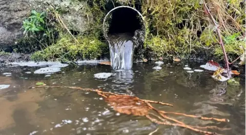 Liquid pouring from an open pipe into a river 